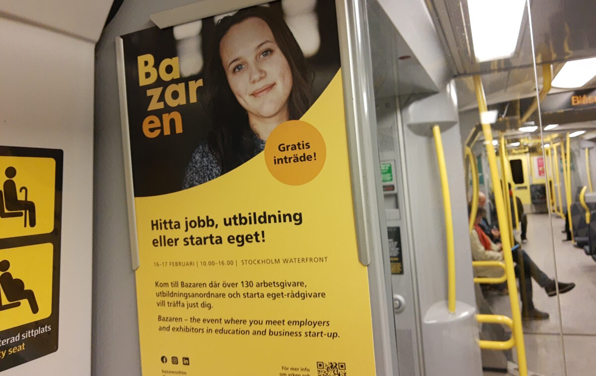 Bild inne i en tunnelbanevagn med fokus på en gulfärgad reklamaffisch för Bazaren - en jobb- och utbildningsmässa.