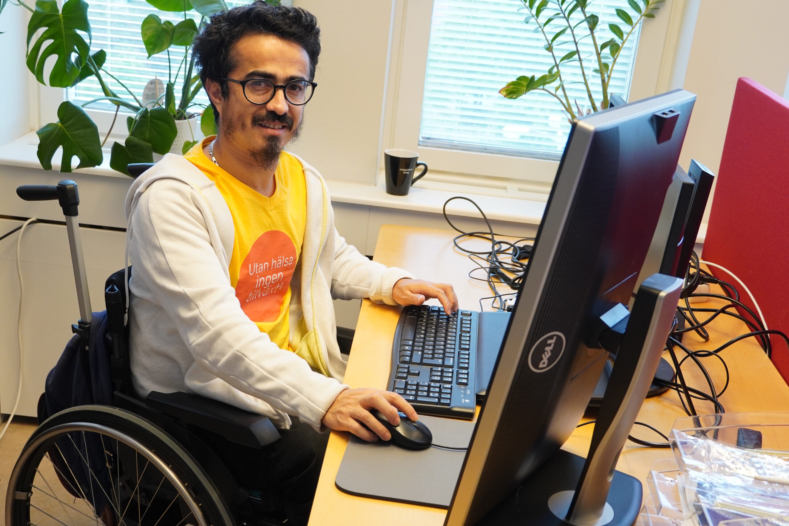 Ashraf sitter och jobbar bakom ett par stora skärmar på kontoret i Farsta. Han tittar upp och ler försiktigt.