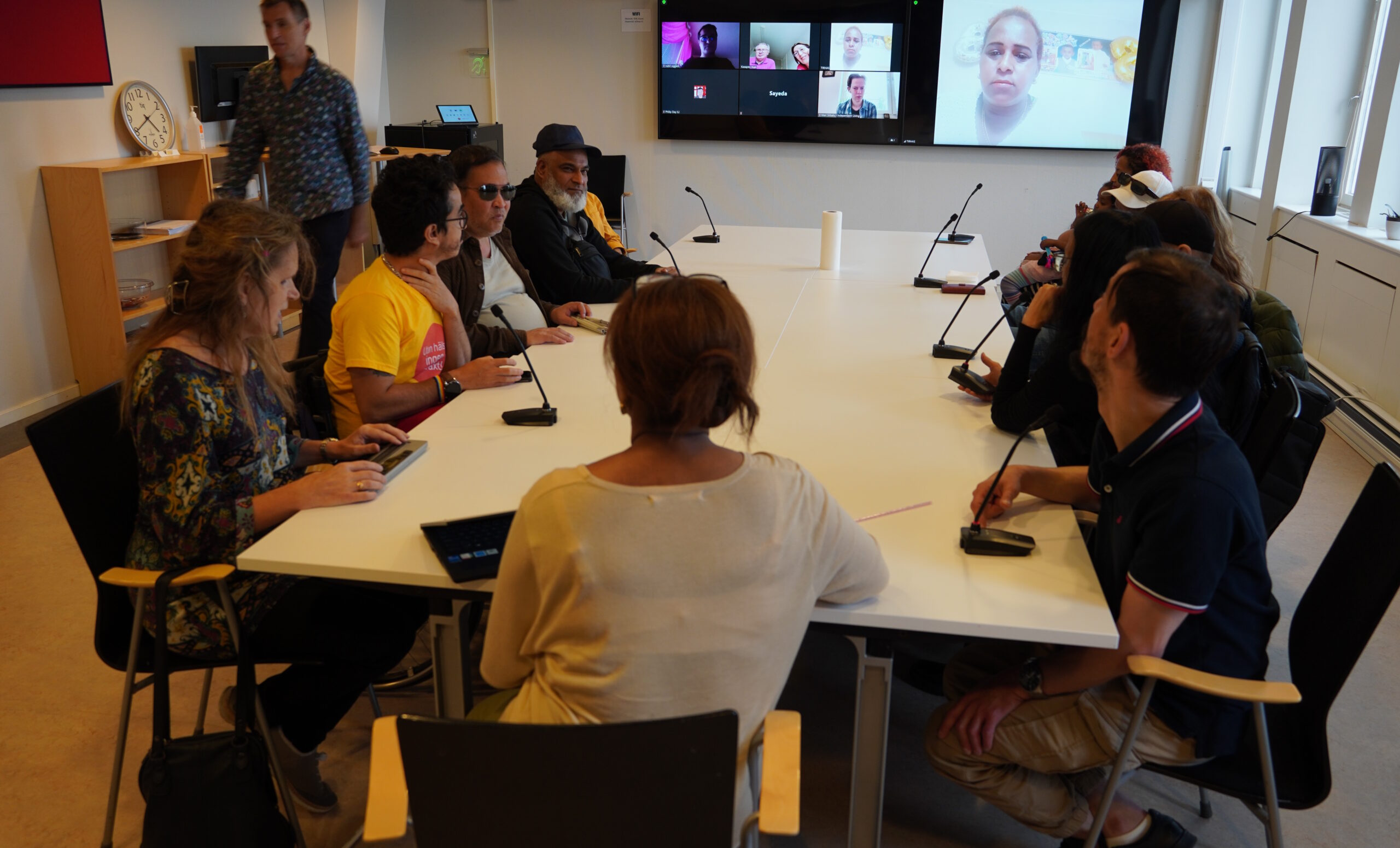 deltagarna samlade kring stora bordet i stora konferensrummet på STIL-kontoret och andra deltagare på skärmarna bakom.