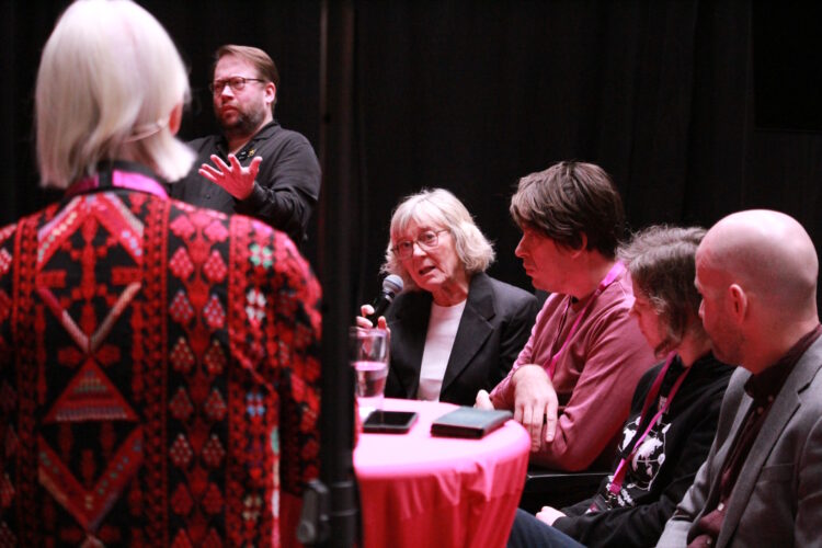 Panelen sedd från sidan. Moderatorn Elna Wahlgren Lundqvist, står till vänster med ryggen mot kameran. 