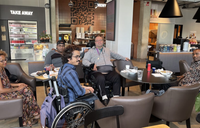 Ashraf och några deltagare sitter kring ett bord på kaféet. I bakgrunden kafédisken. 